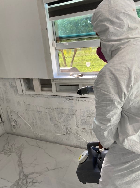 Technician in protective gear fogging an opened-up wall with antimicrobial
