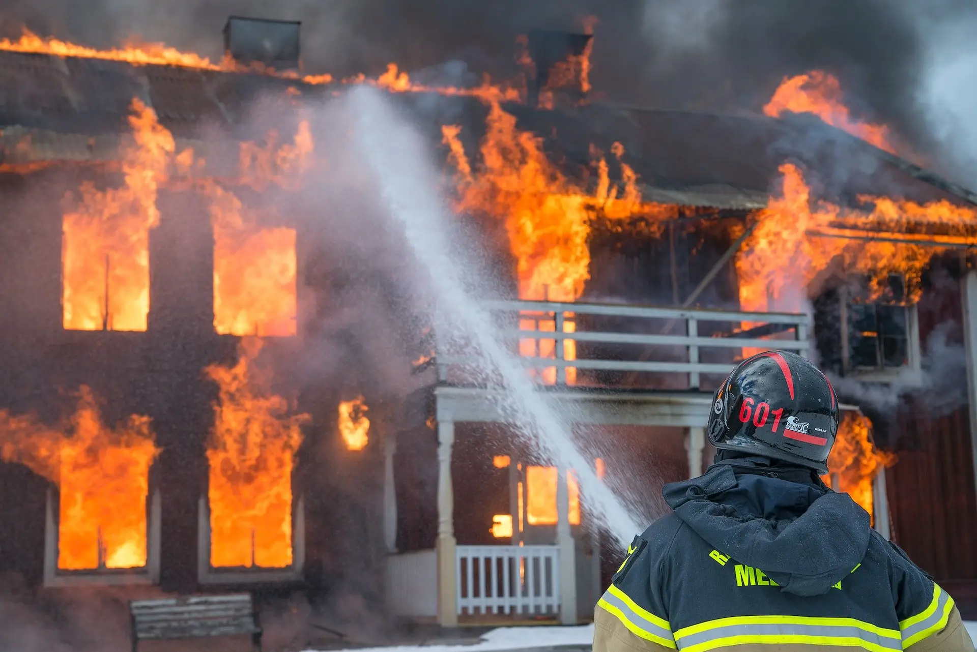 Firefighter spraying water on a house engulfed in flames