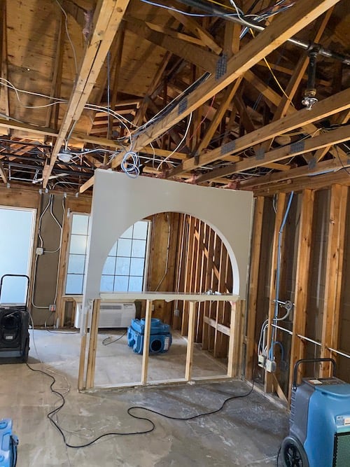 Gutted interior with exposed framing and drying equipment during reconstruction